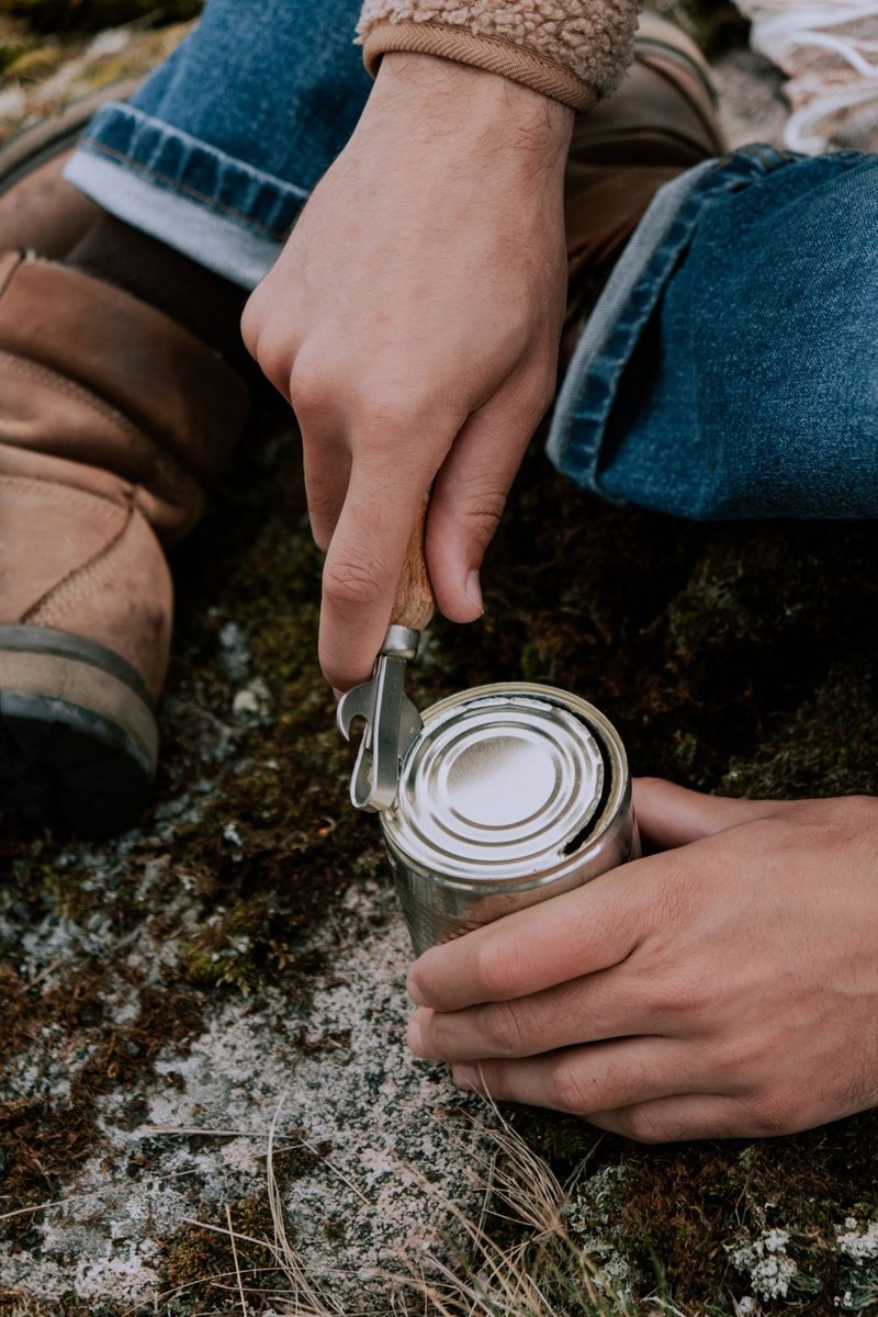 Hands opening a food can with a manual tool