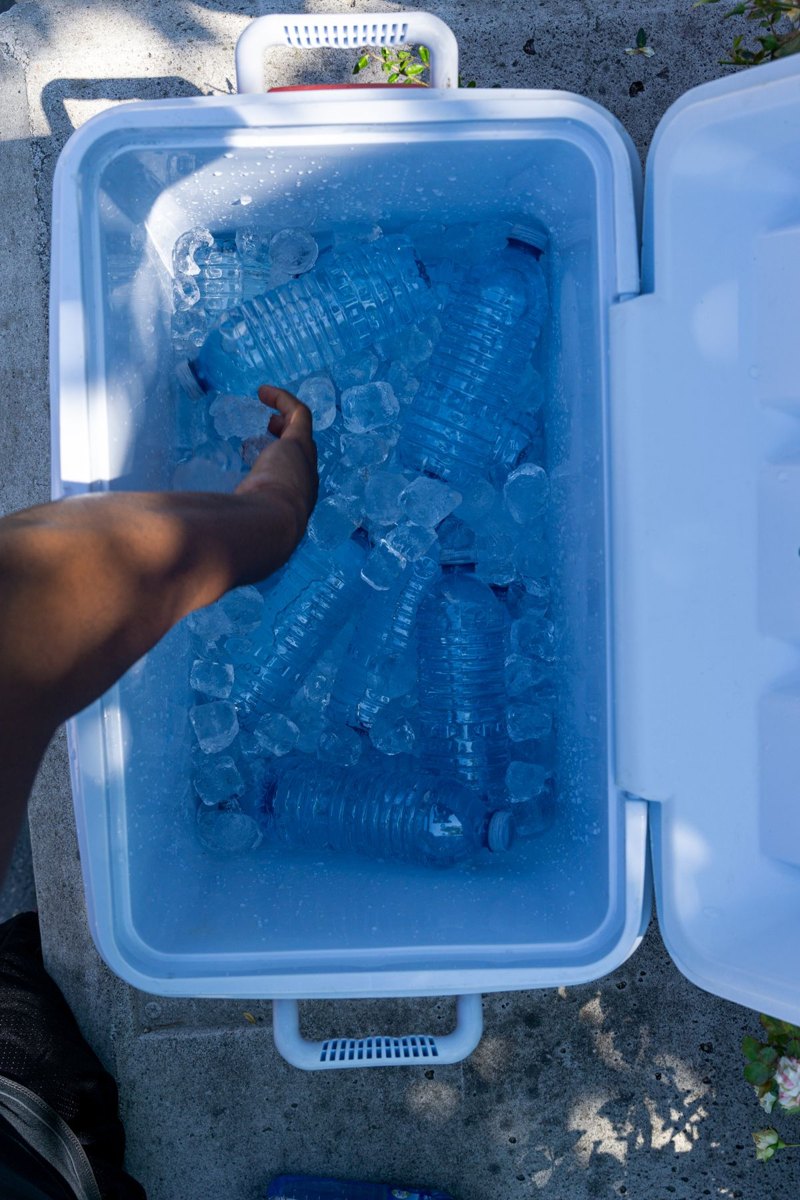 Hand retrieving a water bottle from an ice-filled cooler