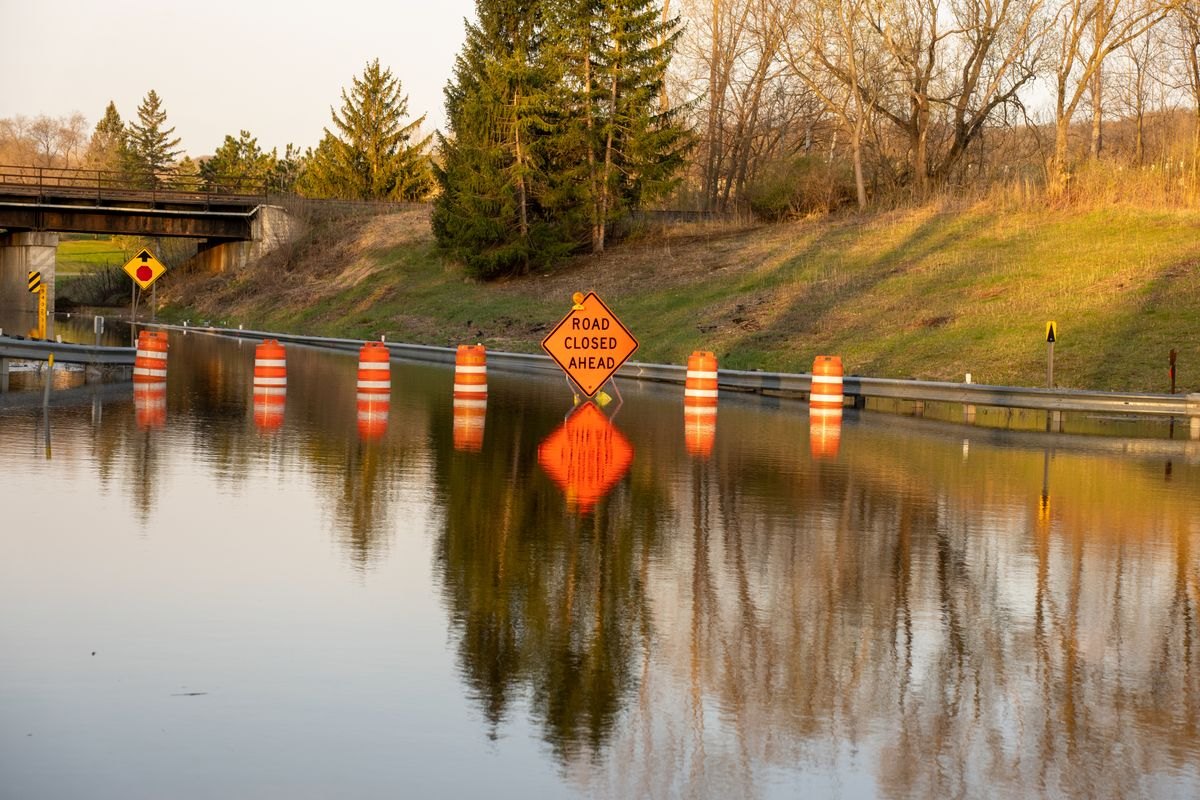 Floodwater covering a closed road beyond warning signs